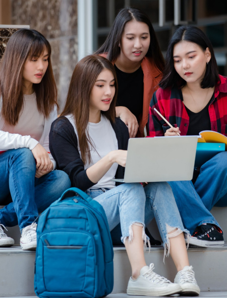 Vier Studentinnen sitzen auf einer Treppe und schauen auf einen Laptop, den eine von ihnen in der Hand hält.